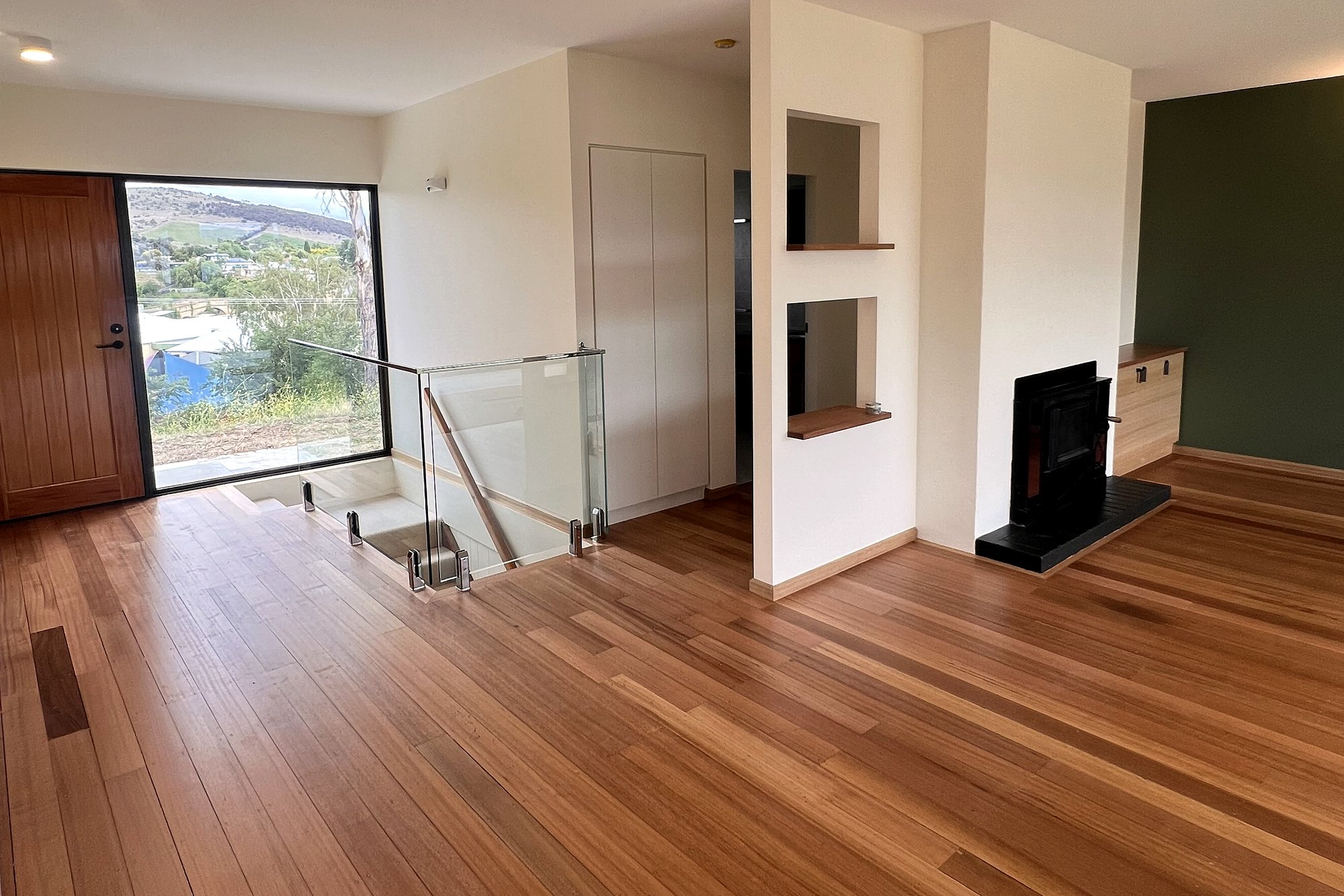Richmond living area with timber entry door, glass balustrade, joinery nook and wood heater, built by LHPL Contracting